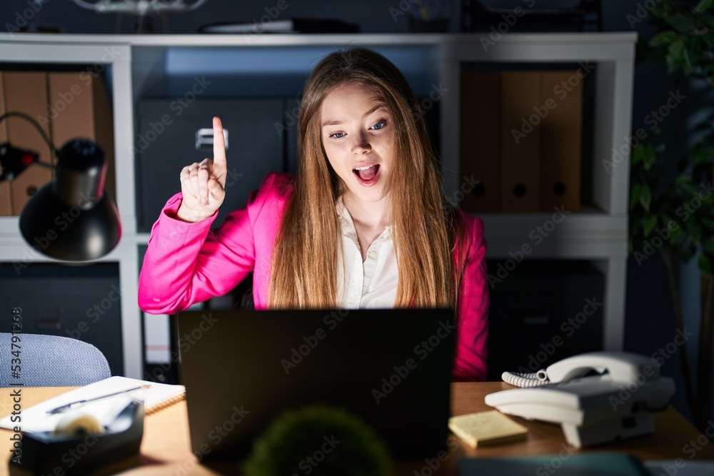 Young caucasian woman working at the office at night pointing finger up with successful idea. exited and happy. number one. Young caucasian woman working at the office at night pointing finger up with successful idea. exited and happy. number one.