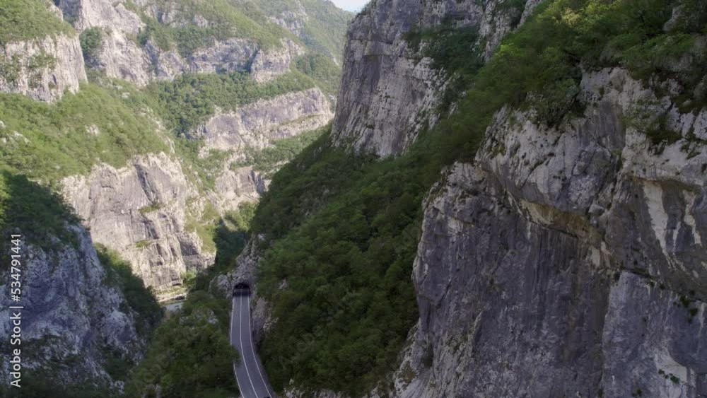 Traffic road with moving trucks coming out of a tunnel in a river gorge shot on a sunny day from the air by a moving drone passing by the canyon cliffs Traffic road with moving trucks coming out of a tunnel in a river gorge shot on a sunny day from the air by a moving drone passing by the canyon cliffs