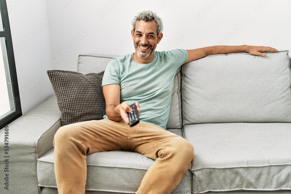 Middle age grey-haired man watching movie sitting on sofa at home Middle age grey-haired man watching movie sitting on sofa at home
