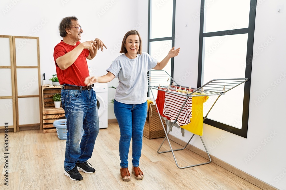 Middle age man and woman couple dancing waiting for washing machine at laundry