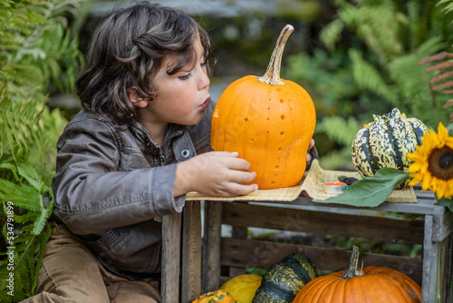 Obraz na plátne Long-haired brown-eyed boy in the garden making a pumpkin mask for Halloween, Au
