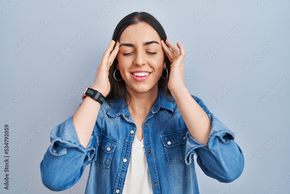 Hispanic woman standing over blue background with hand on head, headache because stress. suffering migraine. Hispanic woman standing over blue background with hand on head, headache because stress. suffering migraine.