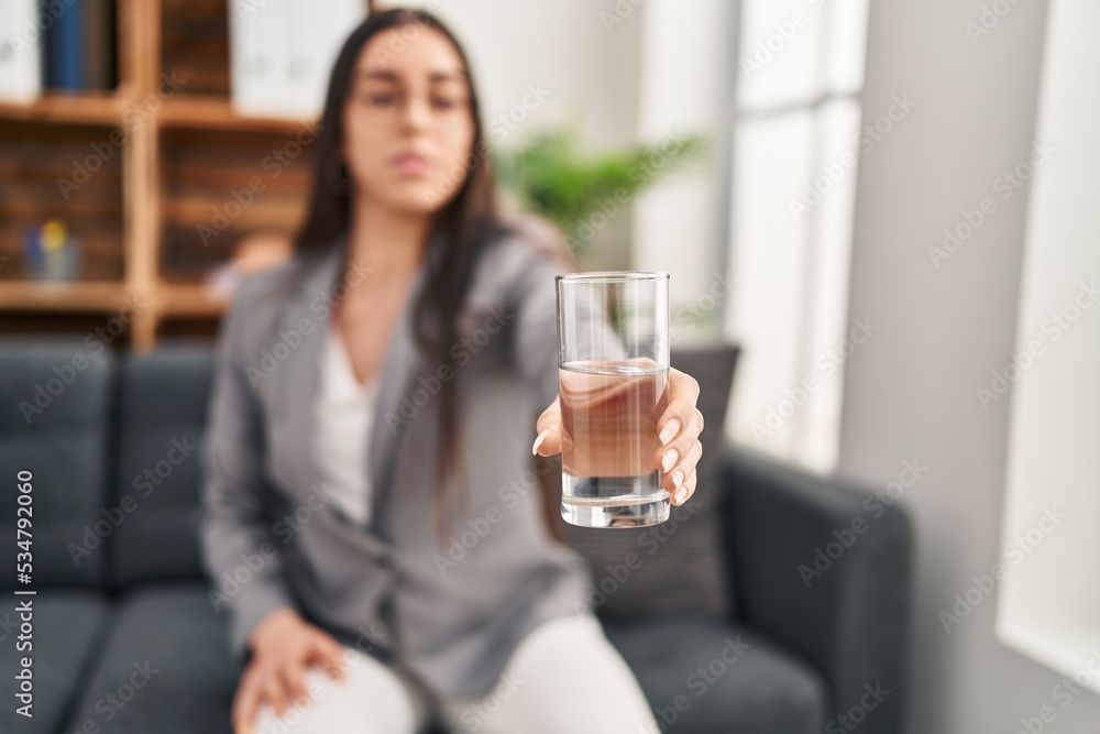 Young beautiful hispanic woman psychologist offering glass of water at psychology clinic Young beautiful hispanic woman psychologist offering glass of water at psychology clinic