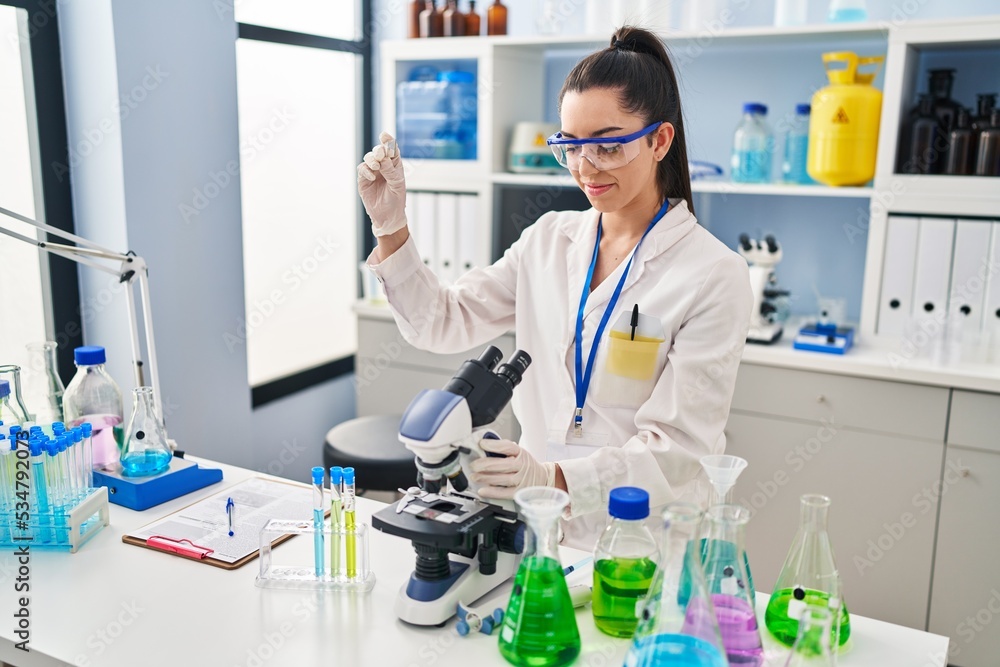 Young beautiful hispanic woman scientist using microscope holding sample at laboratory Young beautiful hispanic woman scientist using microscope holding sample at laboratory