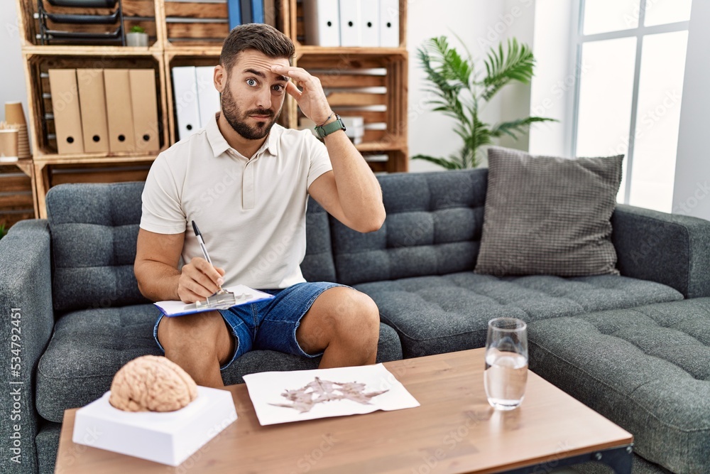 Handsome hispanic man working with rorschach test at psychology clinic worried and stressed about a problem with hand on forehead, nervous and anxious for crisis Handsome hispanic man working with rorschach test at psychology clinic worried and stressed about a problem with hand on forehead, nervous and anxious for crisis