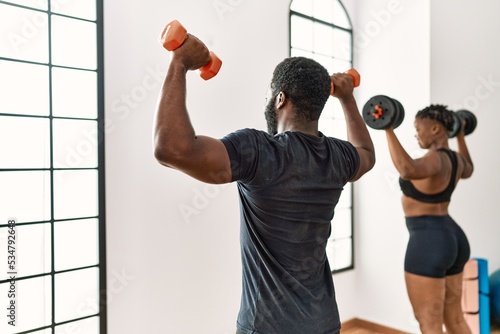 Young african american sporty couple on back view training power exercise using dumbbells at sport center.
