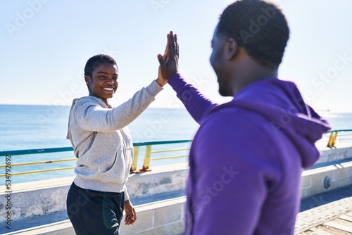 Man and woman couple wearing sportswear high five with hands raised up at seaside