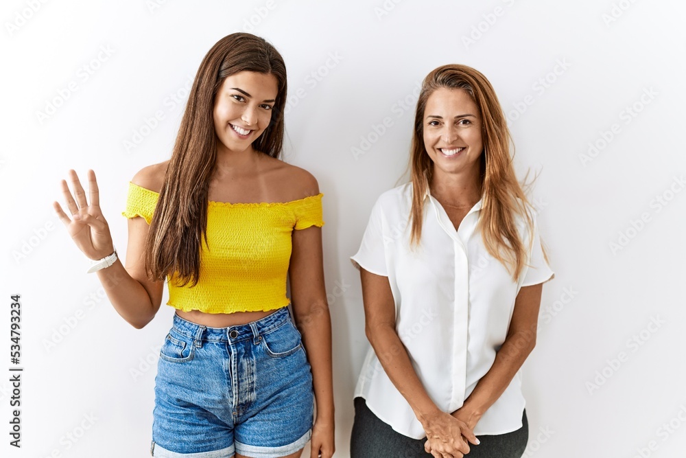 Mother and daughter together standing together over isolated background showing and pointing up with fingers number four while smiling confident and happy.
