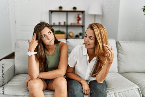 Mother and daughter together sitting on the sofa at home shooting and killing oneself pointing hand and fingers to head like gun, suicide gesture.