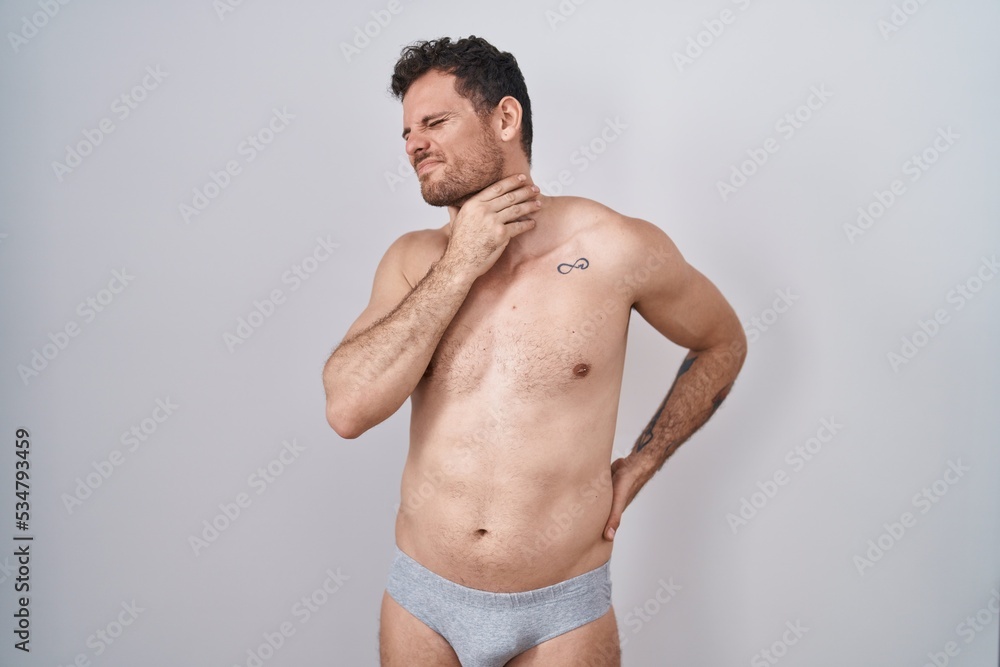 Young hispanic man standing shirtless wearing underware touching painful neck, sore throat for flu, clod and infection Young hispanic man standing shirtless wearing underware touching painful neck, sore throat for flu, clod and infection