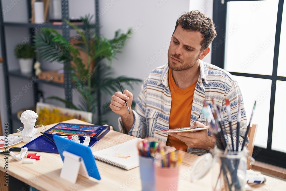 Fototapeta premium Young hispanic man artist having video call drawing at art studio