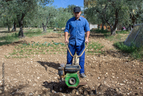 Farmer with a tiller while he tills a land for the cultivation of the vegetable garden. Fertile soil preparation
