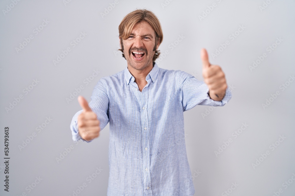Caucasian man with mustache standing over white background approving doing positive gesture with hand, thumbs up smiling and happy for success. winner gesture. Caucasian man with mustache standing over white background approving doing positive gesture with hand, thumbs up smiling and happy for success. winner gesture.