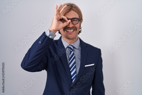 Caucasian man with mustache wearing business clothes doing ok gesture with hand smiling, eye looking through fingers with happy face.