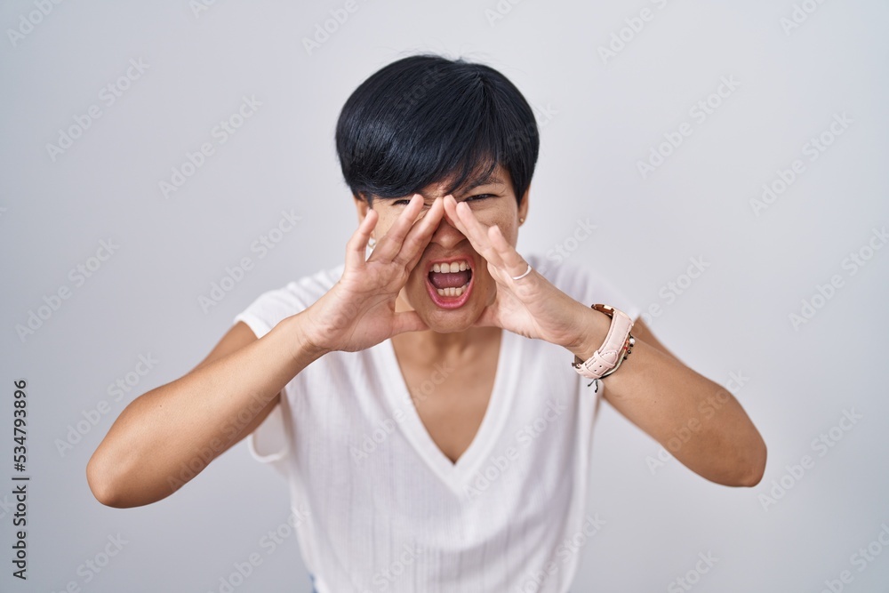 Young asian woman with short hair standing over isolated background shouting angry out loud with hands over mouth Young asian woman with short hair standing over isolated background shouting angry out loud with hands over mouth