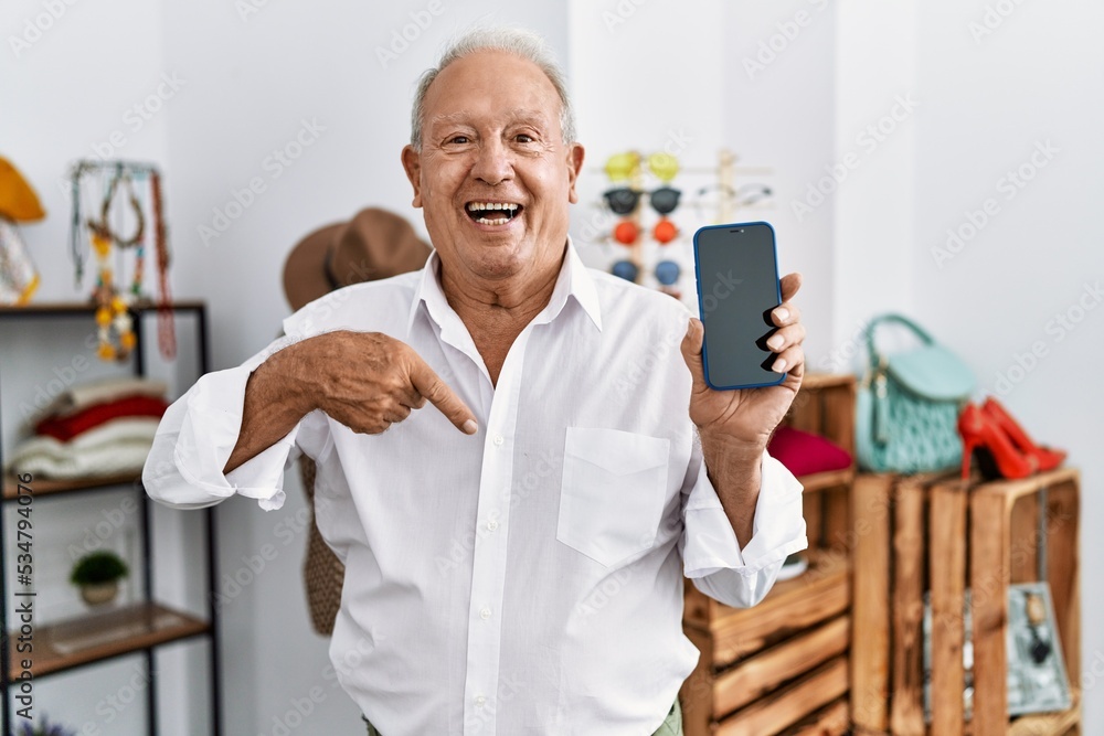 Senior man holding smartphone at retail shop pointing finger to one self smiling happy and proud Senior man holding smartphone at retail shop pointing finger to one self smiling happy and proud