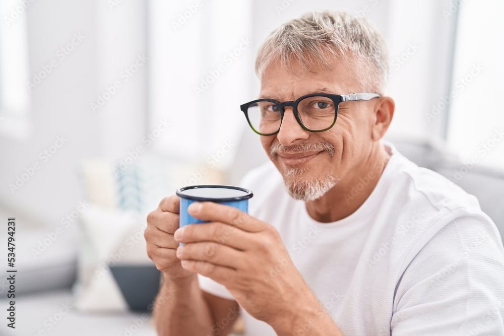 Middle age grey-haired man drinking coffee sitting on sofa at home Middle age grey-haired man drinking coffee sitting on sofa at home
