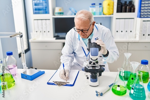 Senior man wearing scientist uniform using microscope at laboratory