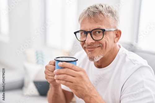 Middle age grey-haired man drinking coffee sitting on sofa at home
