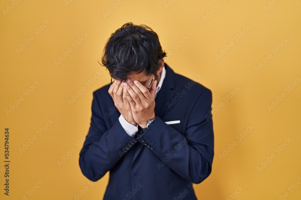 Handsome latin man standing over yellow background with sad expression covering face with hands while crying. depression concept. Handsome latin man standing over yellow background with sad expression covering face with hands while crying. depression concept.