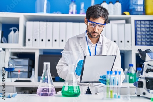 Young hispanic man scientist write on clipboard at laboratory