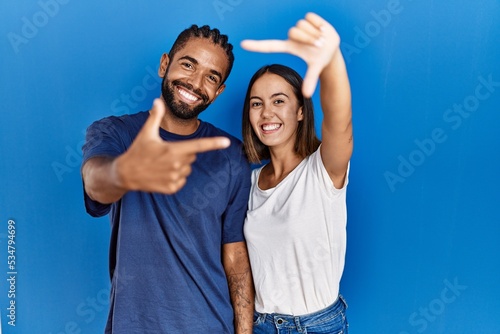 Young hispanic couple standing together smiling making frame with hands and fingers with happy face. creativity and photography concept.