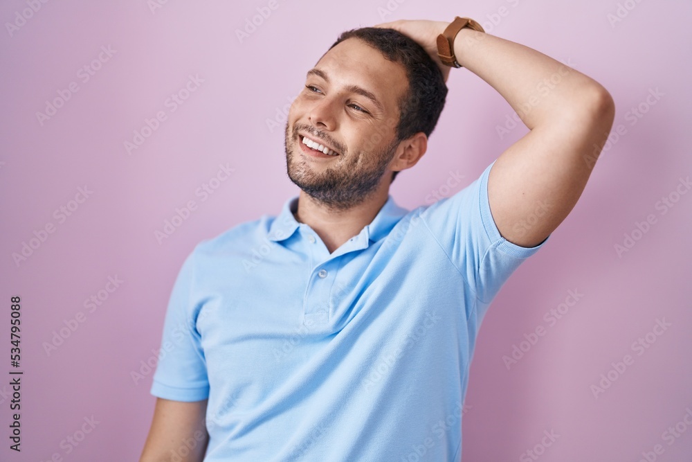 Hispanic man standing over pink background smiling confident touching hair with hand up gesture, posing attractive and fashionable Hispanic man standing over pink background smiling confident touching hair with hand up gesture, posing attractive and fashionable