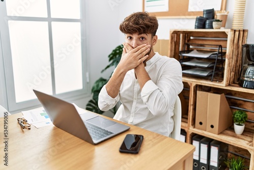 Young arab man working using computer laptop at the office shocked covering mouth with hands for mistake. secret concept.