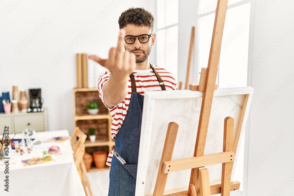Arab young man at art studio showing middle finger, impolite and rude fuck off expression Arab young man at art studio showing middle finger, impolite and rude fuck off expression