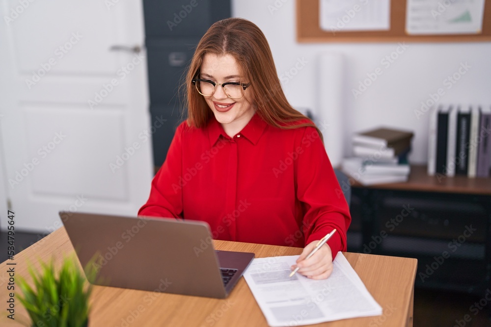Young redhead woman business worker using laptop writing document at office Young redhead woman business worker using laptop writing document at office