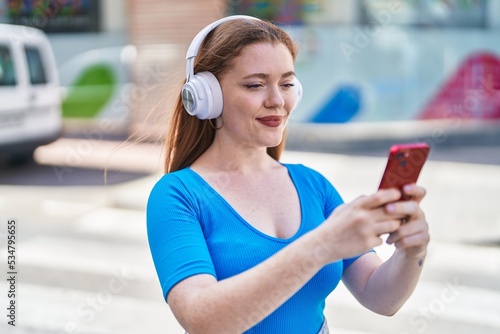 Young redhead woman listening to music at street