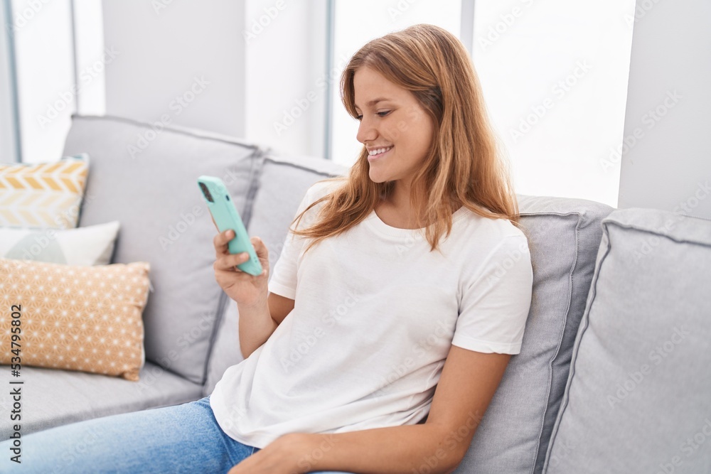 Young blonde girl using smartphone sitting on sofa at home Young blonde girl using smartphone sitting on sofa at home