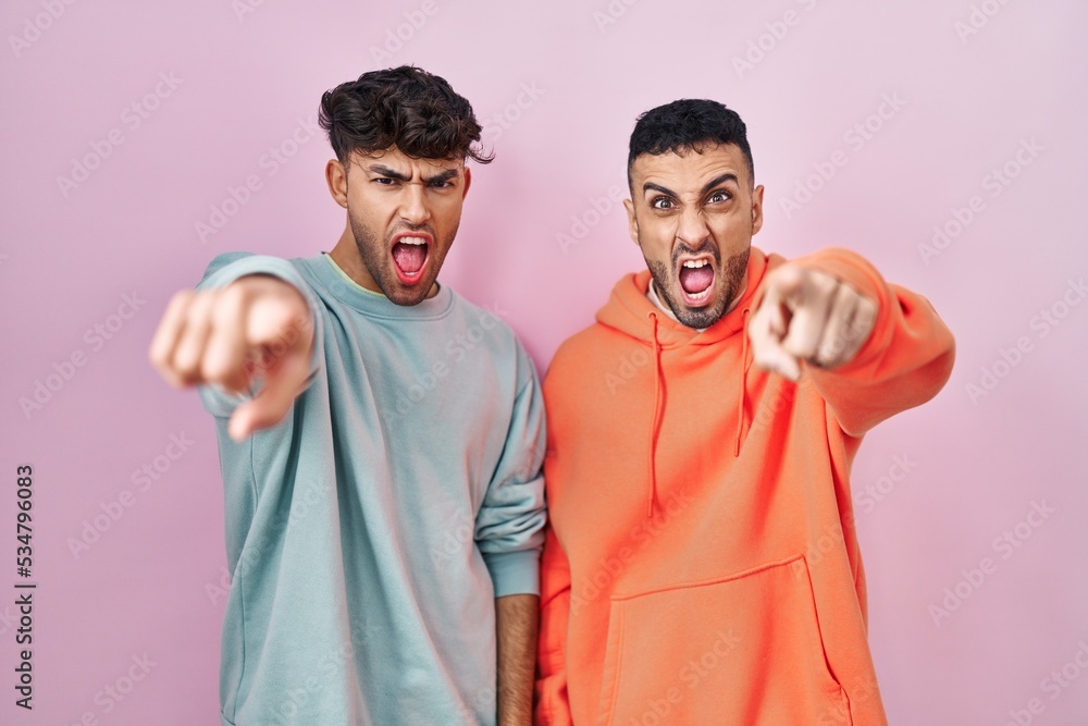 Young hispanic gay couple standing over pink background pointing displeased and frustrated to the camera, angry and furious with you Young hispanic gay couple standing over pink background pointing displeased and frustrated to the camera, angry and furious with you