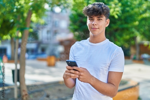 Young hispanic teenager smiling confident using smartphone at park photo