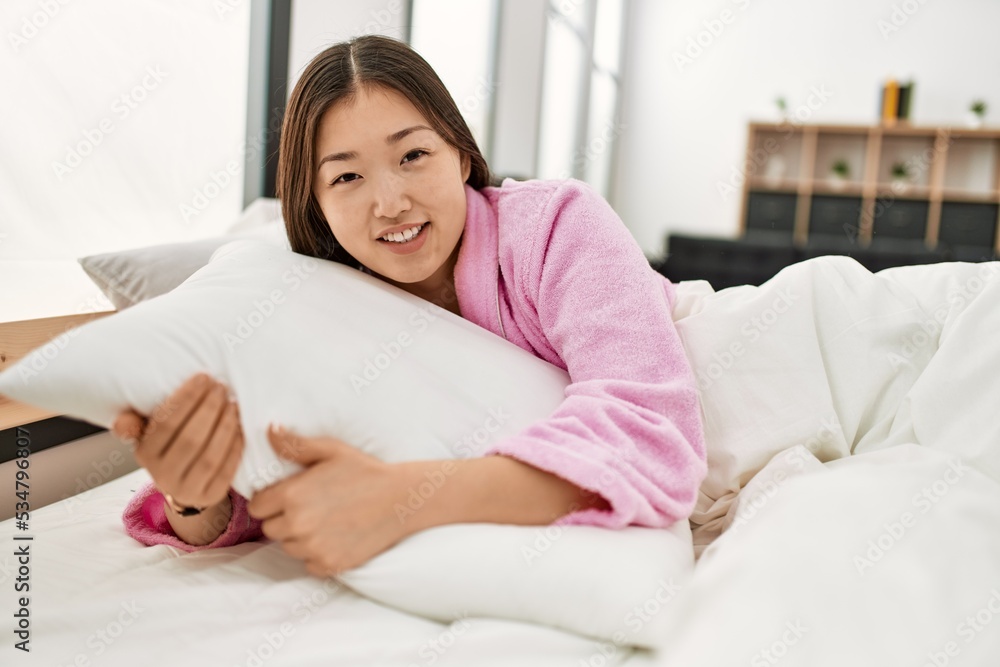 ¡Young chinese girl smiling happy and hugging pillow lying on the bed at bedroom. ¡Young chinese girl smiling happy and hugging pillow lying on the bed at bedroom.