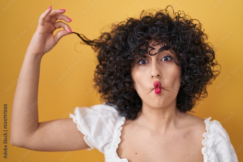 Young brunette woman with curly hair holding curl making fish face with mouth and squinting eyes, crazy and comical. Young brunette woman with curly hair holding curl making fish face with mouth and squinting eyes, crazy and comical.