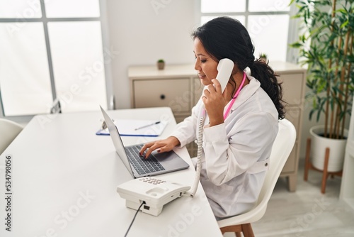Young chinese woman wearing doctor uniform talking on the telephone at clinic