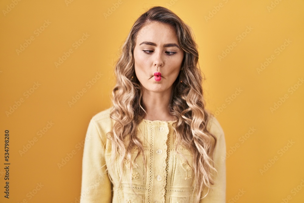 Young caucasian woman standing over yellow background making fish face with lips, crazy and comical gesture. funny expression. Young caucasian woman standing over yellow background making fish face with lips, crazy and comical gesture. funny expression.