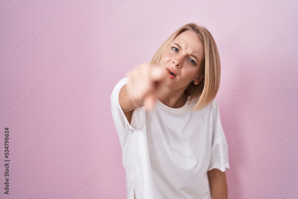 Young caucasian woman standing over pink background pointing displeased and frustrated to the camera, angry and furious with you Young caucasian woman standing over pink background pointing displeased and frustrated to the camera, angry and furious with you