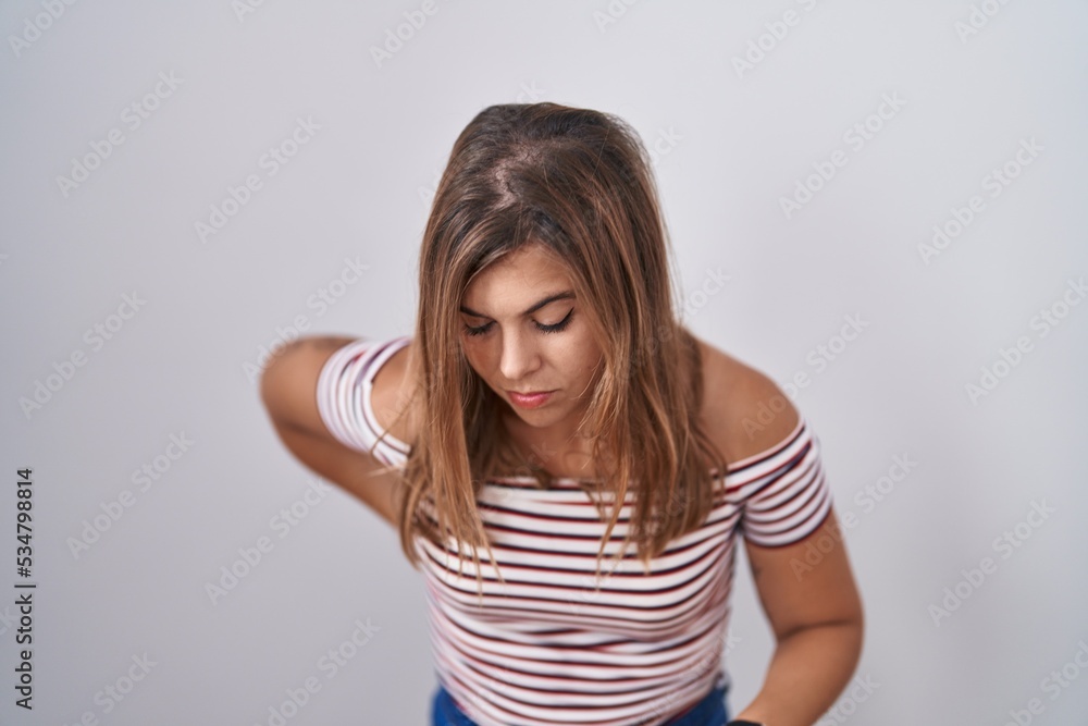 Young hispanic woman standing over isolated background suffering of backache, touching back with hand, muscular pain Young hispanic woman standing over isolated background suffering of backache, touching back with hand, muscular pain