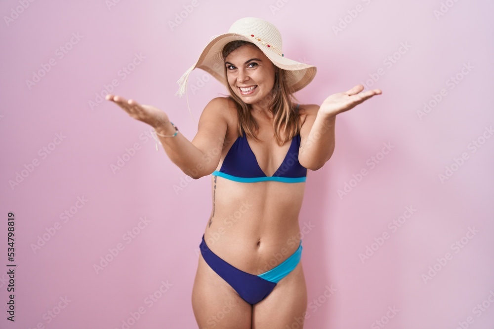 Young hispanic woman wearing bikini over pink background smiling cheerful offering hands giving assistance and acceptance. Young hispanic woman wearing bikini over pink background smiling cheerful offering hands giving assistance and acceptance.