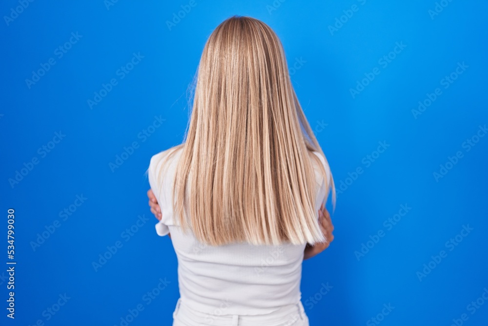 Young caucasian woman standing over blue background standing backwards looking away with crossed arms Young caucasian woman standing over blue background standing backwards looking away with crossed arms