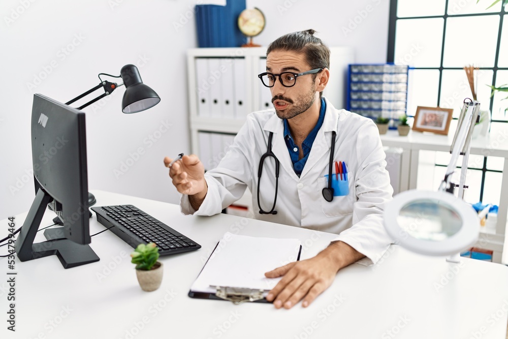 Fototapeta premium Handsome hispanic man working as doctor speaking to a patient at hospital clinic