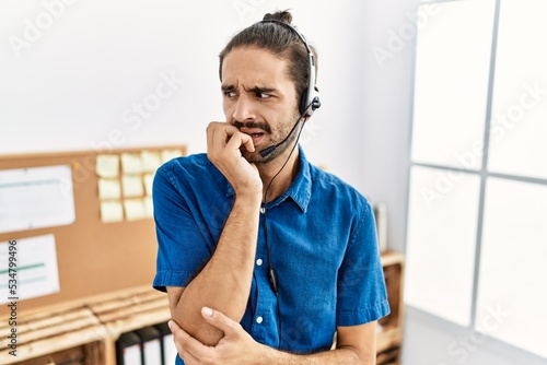 Schilderij op canvas Young hispanic man with beard wearing call center agent headset at the office looking stressed and nervous with hands on mouth biting nails
