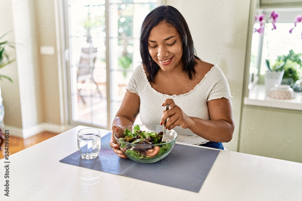 Hispanic brunette woman eating green salad at the kitchen Hispanic brunette woman eating green salad at the kitchen