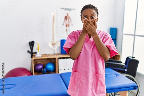 Young african american woman working at pain recovery clinic shocked covering mouth with hands for mistake. secret concept.