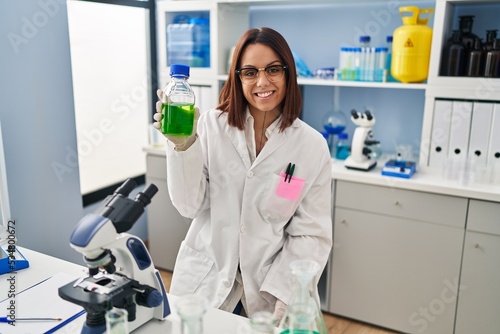 Young beautiful hispanic woman scientist smiling confident measuring liquid at laboratory