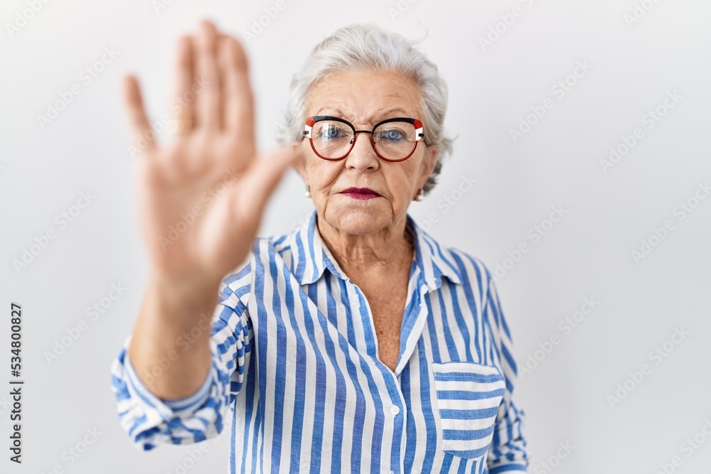 Senior woman with grey hair standing over white background doing stop sing with palm of the hand. warning expression with negative and serious gesture on the face. Senior woman with grey hair standing over white background doing stop sing with palm of the hand. warning expression with negative and serious gesture on the face.