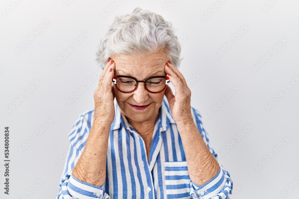 Senior woman with grey hair standing over white background with hand on head for pain in head because stress. suffering migraine. Senior woman with grey hair standing over white background with hand on head for pain in head because stress. suffering migraine.