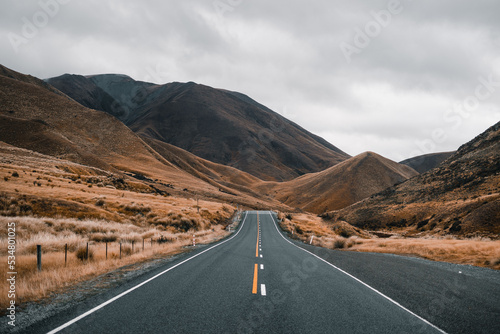 long narrow road without traffic getting lost among the lonely high mountains in a desolate treeless landscape with lots of gray clouds, mount cook, new zealand photo